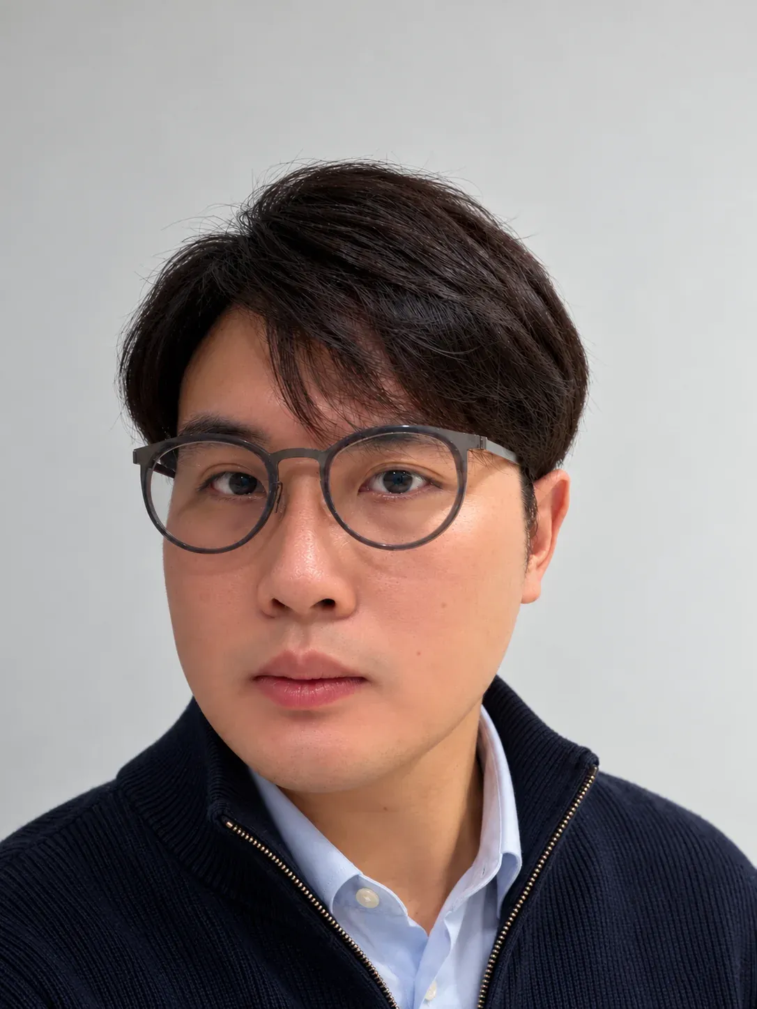 宾震华的肖像：戴圆框眼镜，穿深色针织外套，背景是浅灰色墙面。